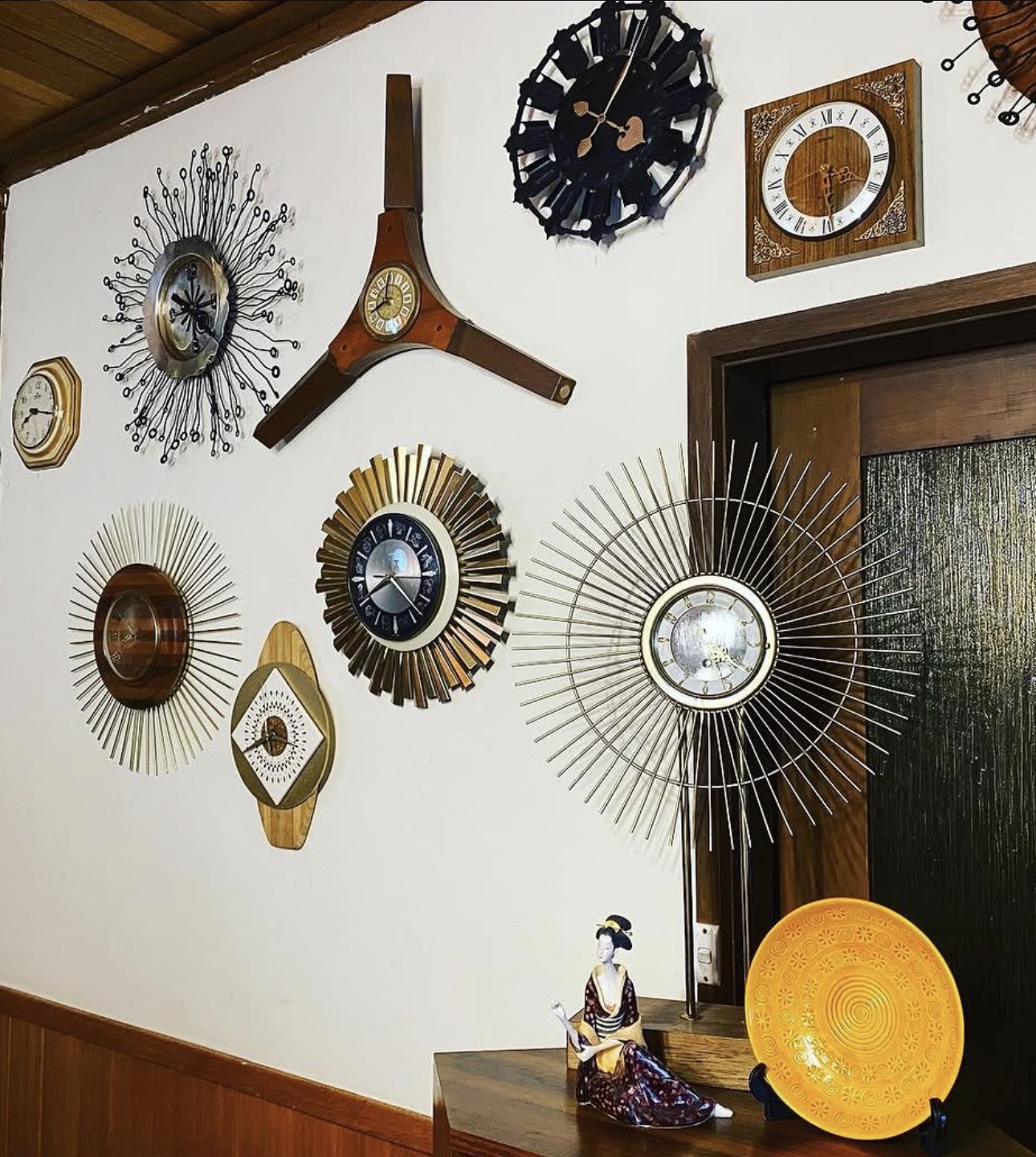 A floor-to-ceiling wall of mid-century sunburst and starburst clocks in walnut, brass and black — part of the Lamptime archive.