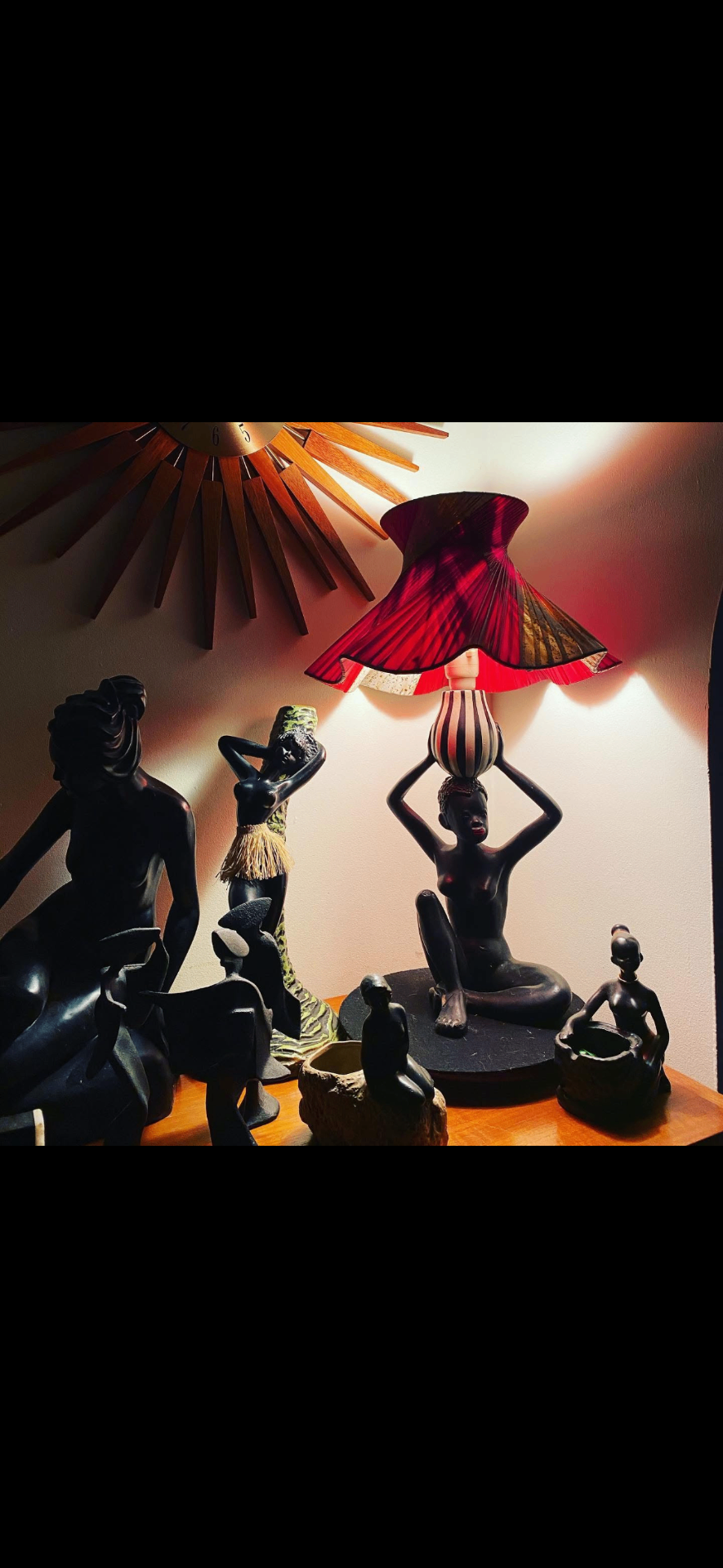 Sculptural Barsony-era figurine grouping with a deep red pleated shade lamp glowing over ebony forms.